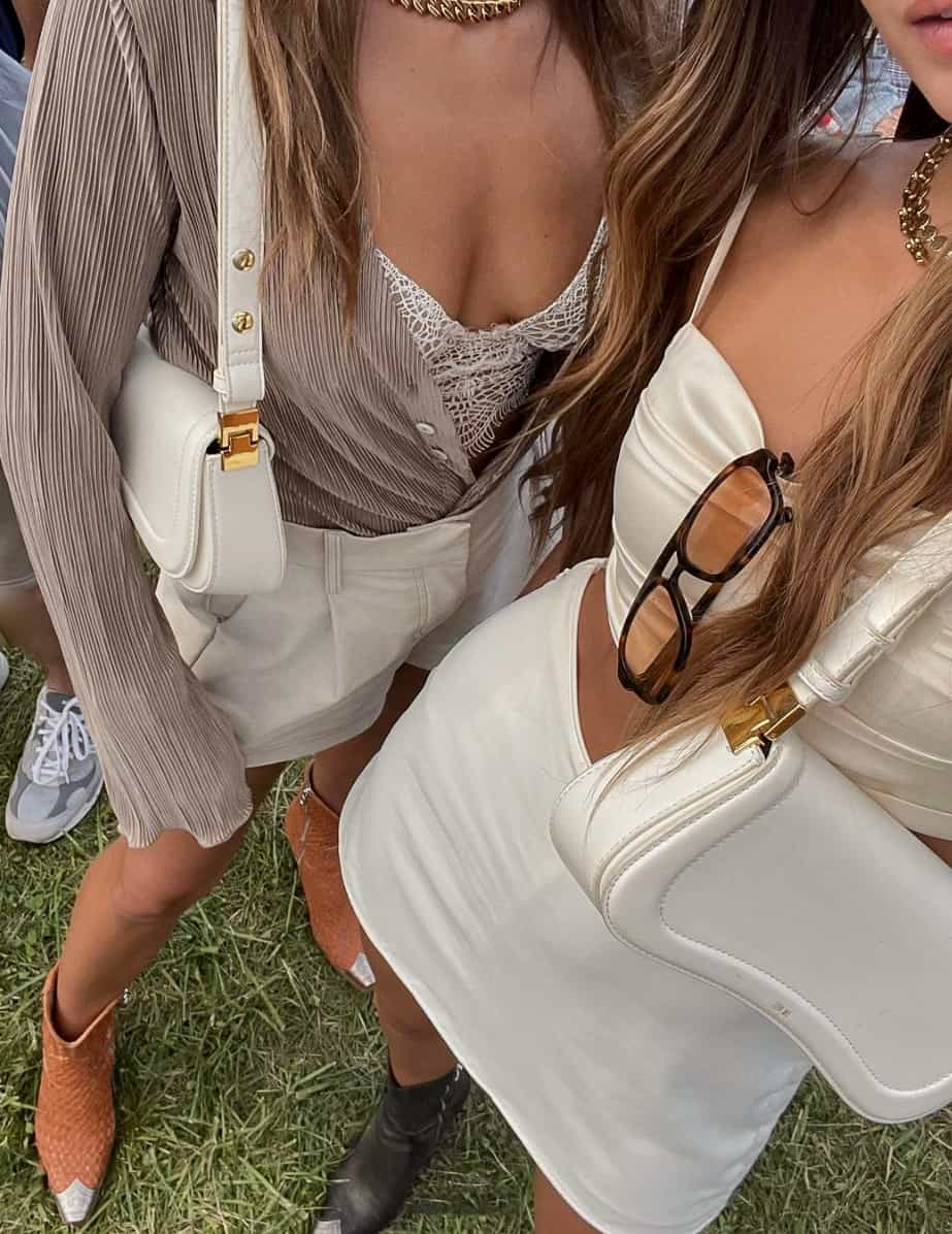 An overhead shot of two women wearing concert outfits, one wearing a white mini skirt and silky white crop top with black boots and the other wearing white shorts with a lacy corset top, a beige cardigan, and orange and silver cowboy boots