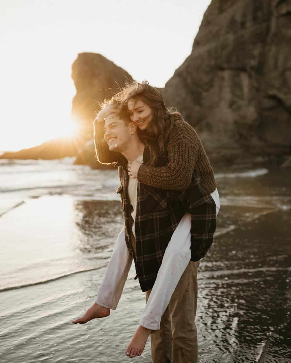 A couple during their engagement photos, the woman is wearing white pants and a brown knit sweater while the man swears tan khakis and a plaid shirt