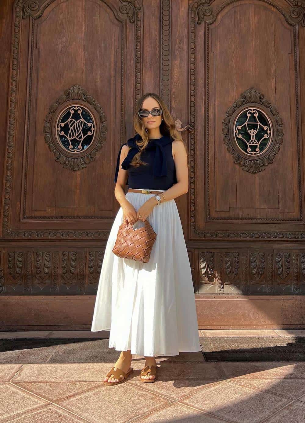 woman wearing a black tank top, tan belt, and full white cotton maxi skirt with brown sandals