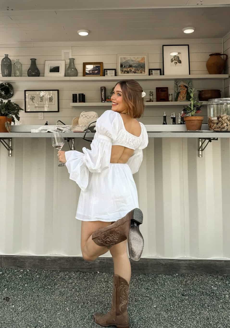 woman wearing a puff sleeve white mini dress with cowboy boots at a winery 
