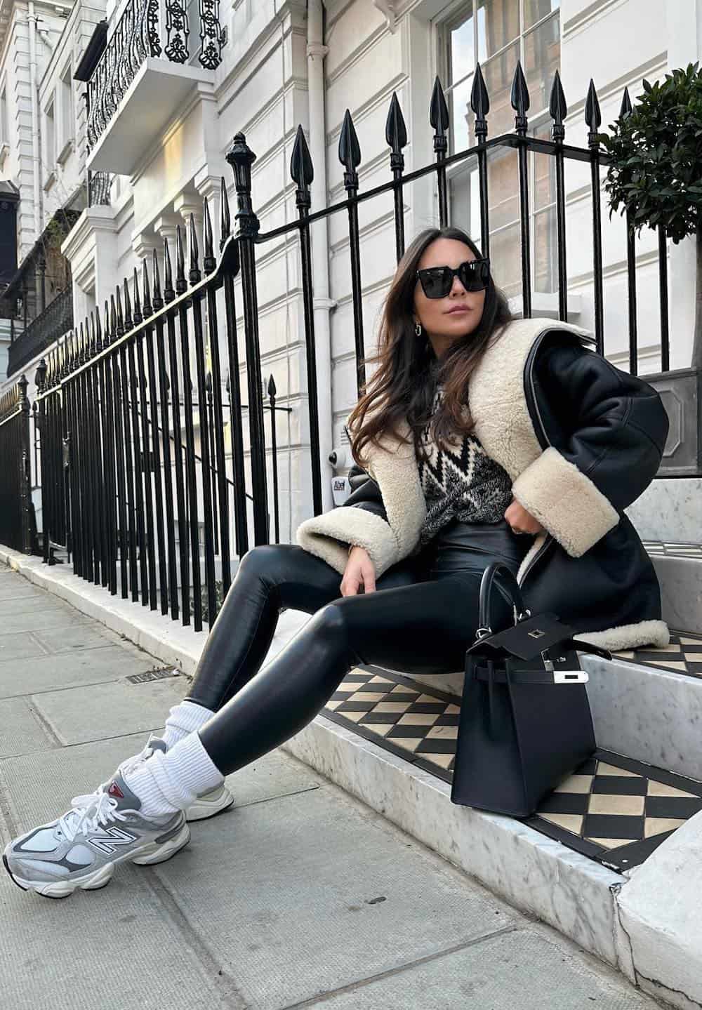 woman wearing an oversized shearling jacket with a knit sweater, leather leggings, and sneakers