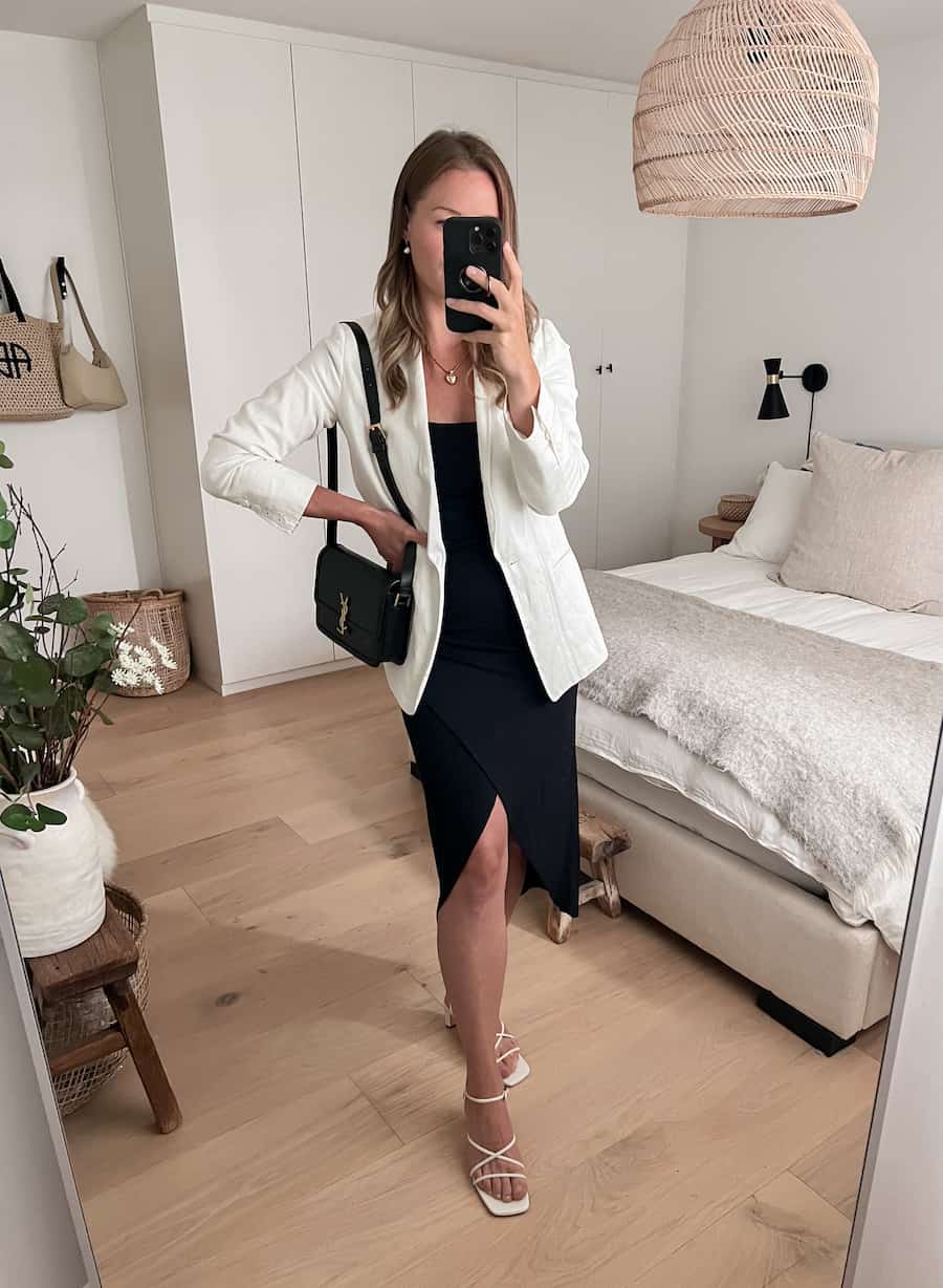 Woman wearing a white linen blazer with a black midi dress and white strappy sandals