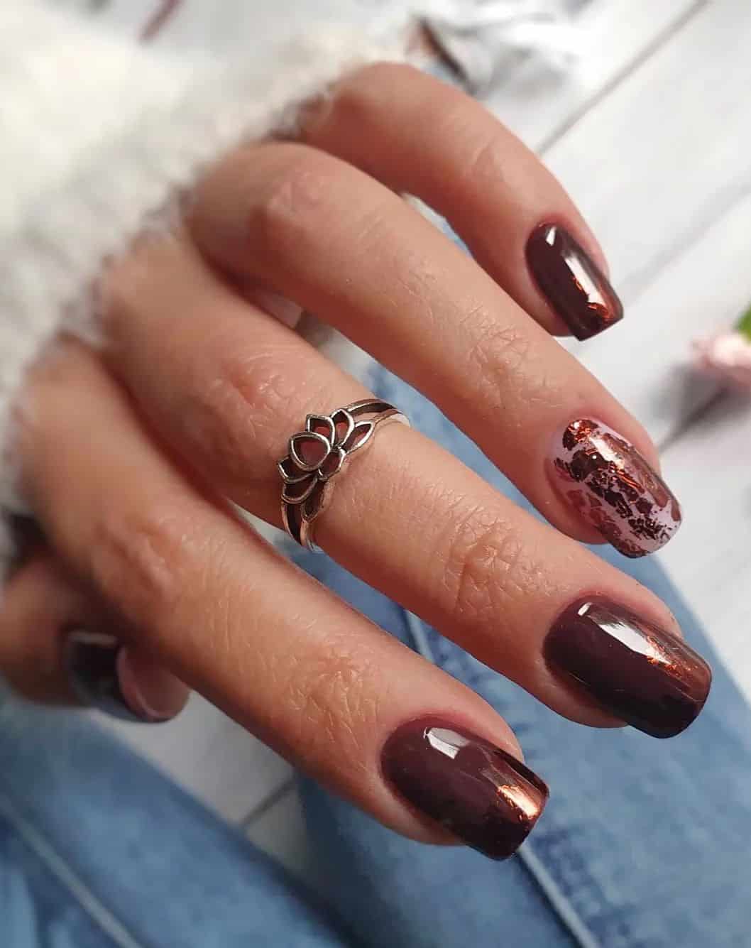 A hand with short squoval nails painted a glossy brown with a metallic brown flake accent nail