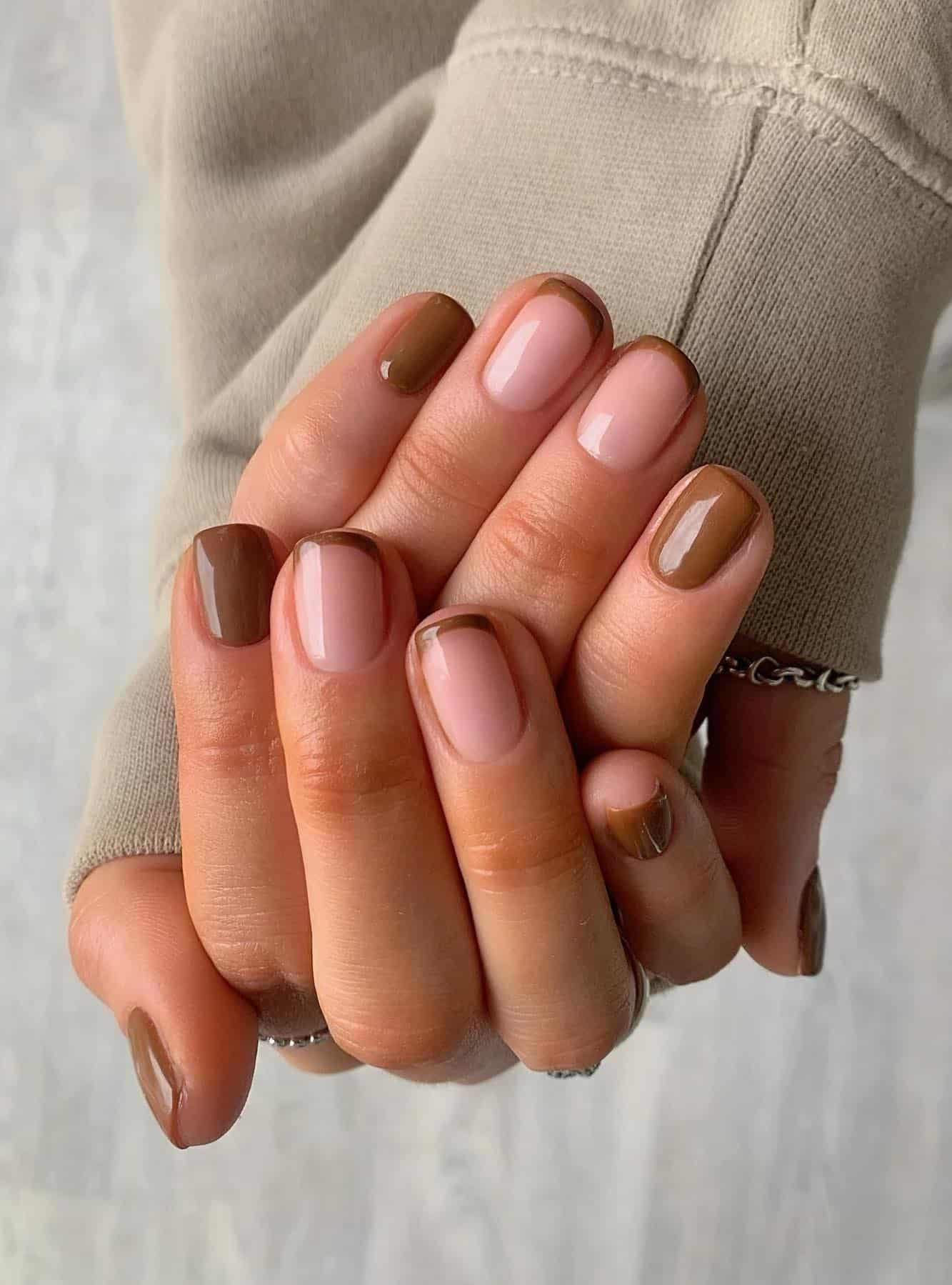 A hand with short squoval nails that have brown French tip accent nails with solid-colored brown nails