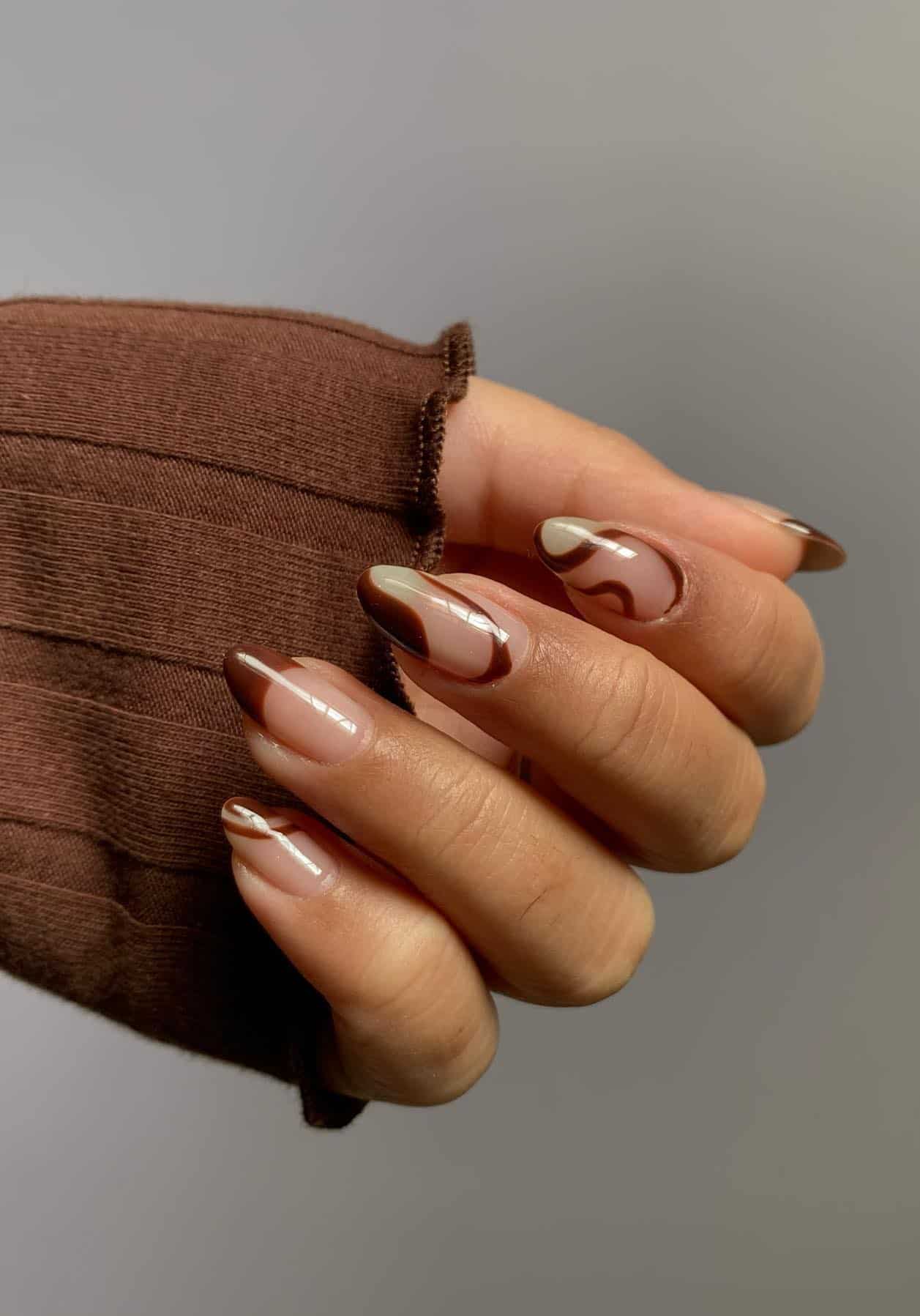 A hand with medium nude nails painted with brown swirls and brown French tips