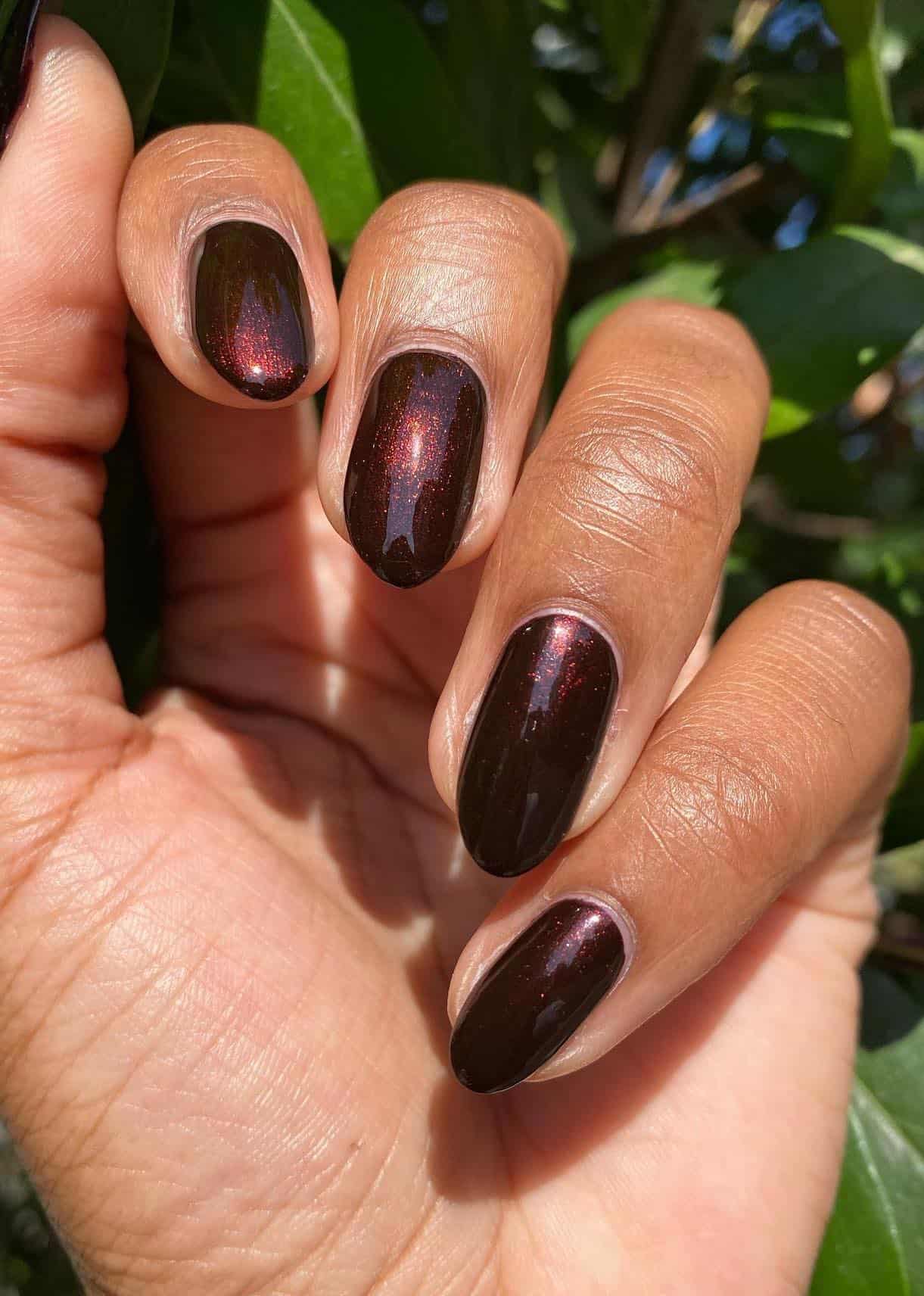 A hand with short almond nails painted with a shimmering dark brown nail polish