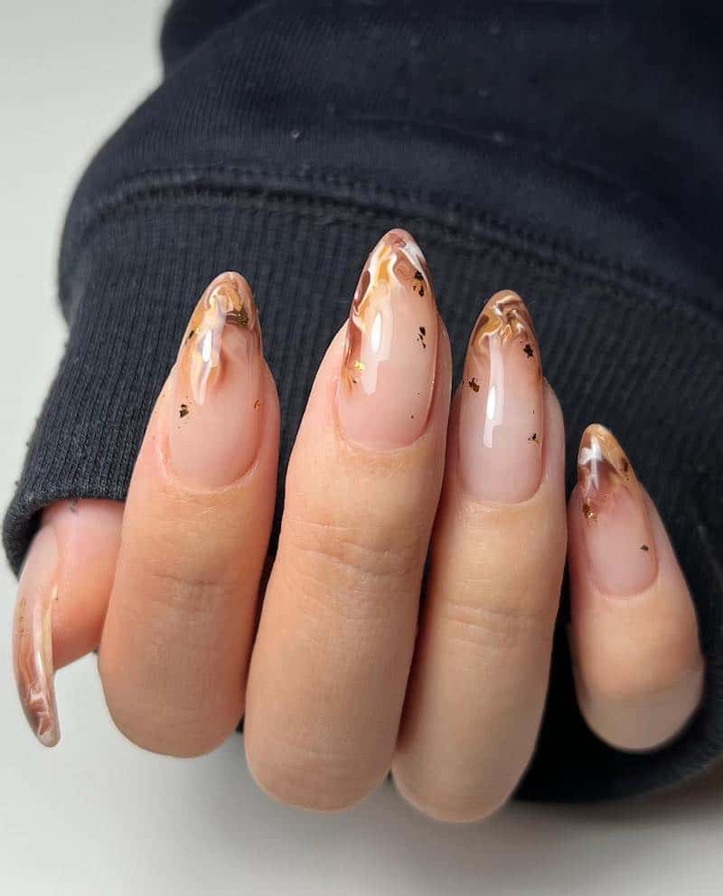 A hand with medium almond nails painted with marbled brown and white French tips with black speckles
