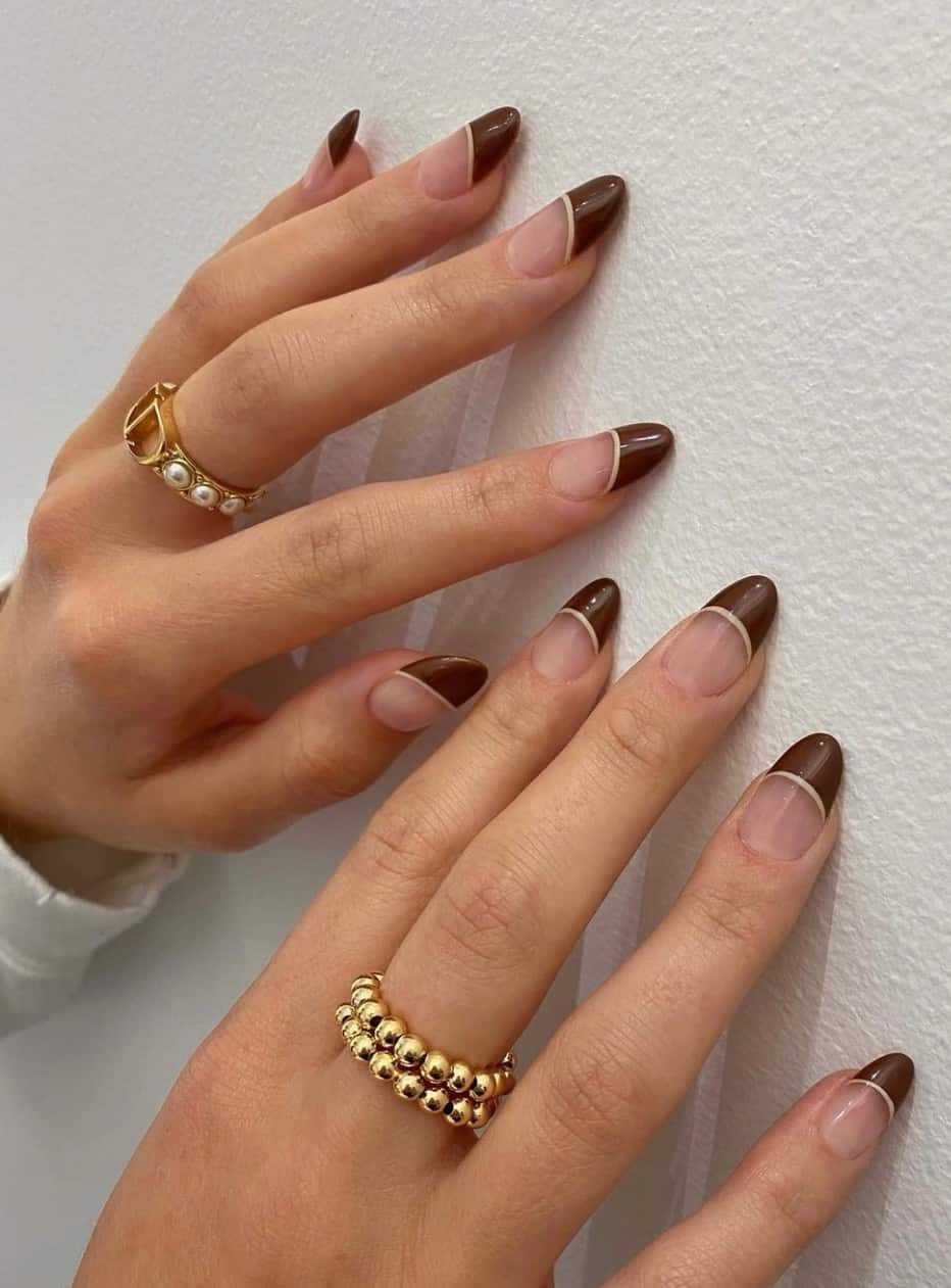 A hand with short almond nails painted with brown French tips with beige borders
