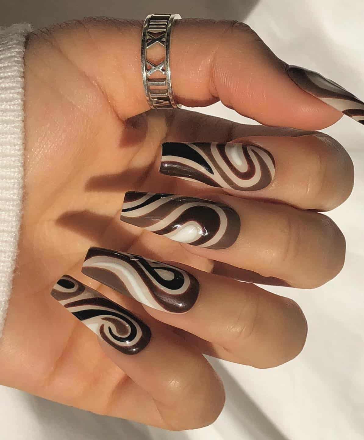 A hand with long coffin nails painted in white, brown, beige, and black swirls