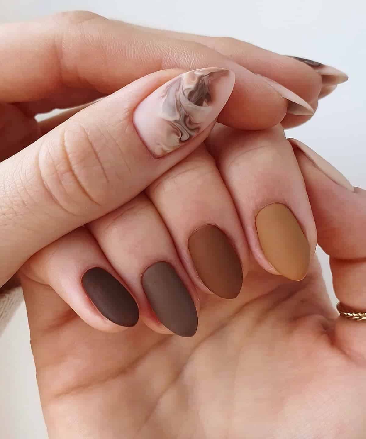 Two hands with short stiletto nails, one painted a brown and beige matte gradient design and the other with white and brown marbled polish