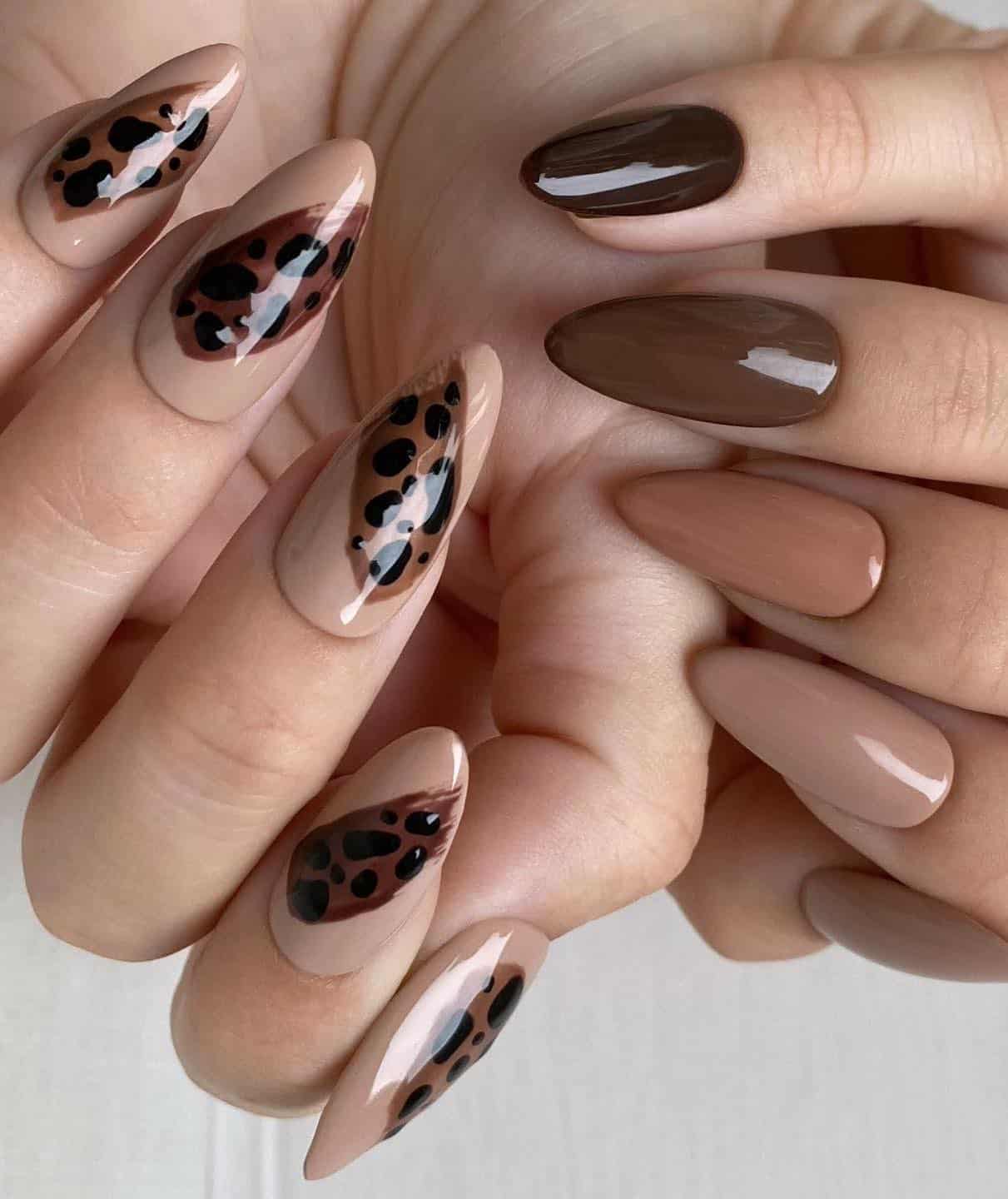 Two hands with medium almond nails painted a brown and beige gradient design on one hand, and the other painted a beige color with brown animal print nail art.