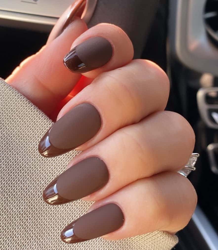 A hand with long almond nails painted a matte brown with glossy French tips