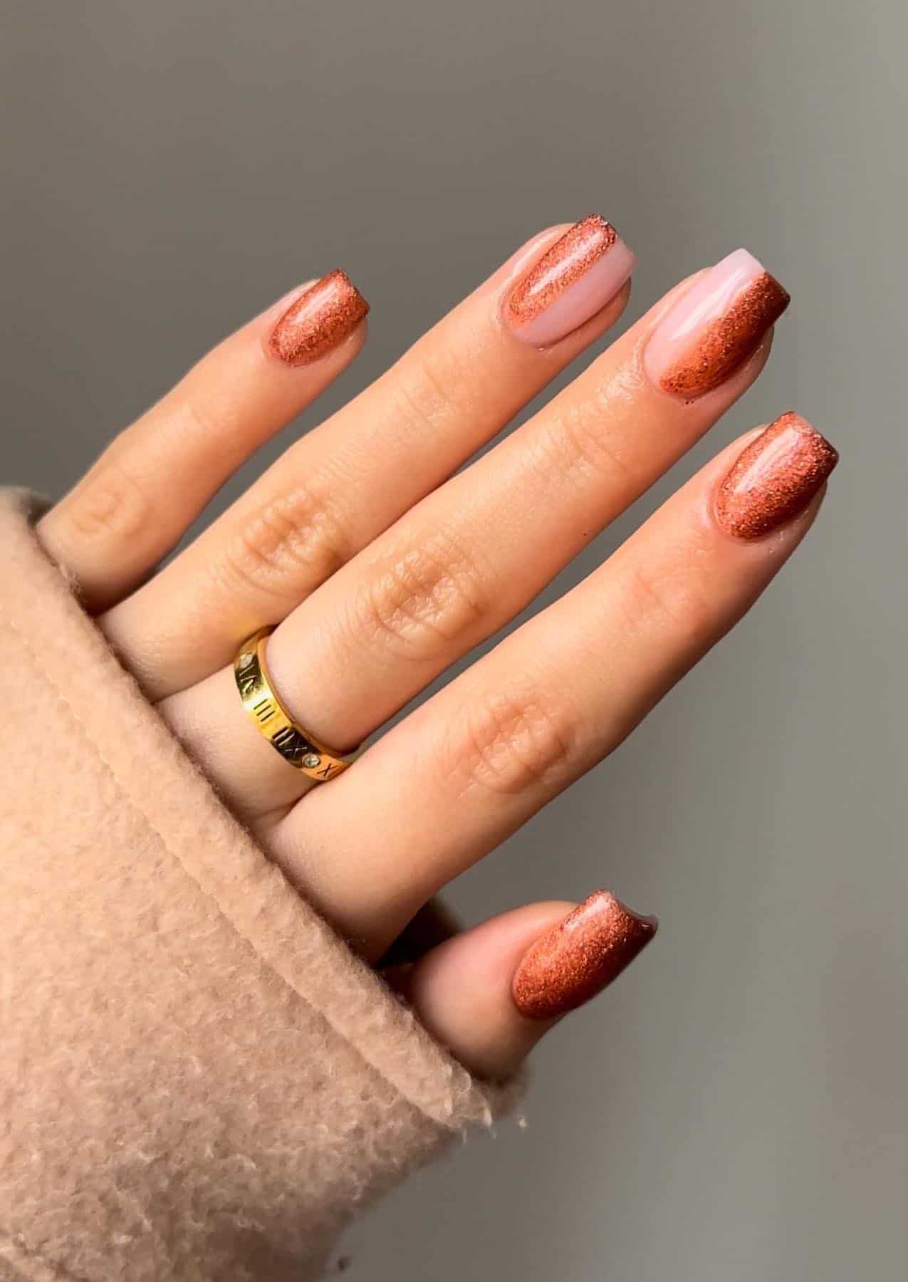 a hand with glittery burnt orange polish with accent nails featuring half polish and half glossy nude