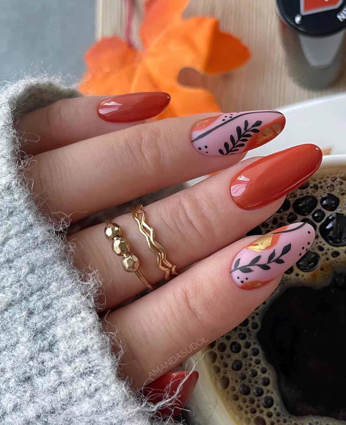a hand with long almond nails painted in glossy burnt orange and matte pink with black botanical art and gold details