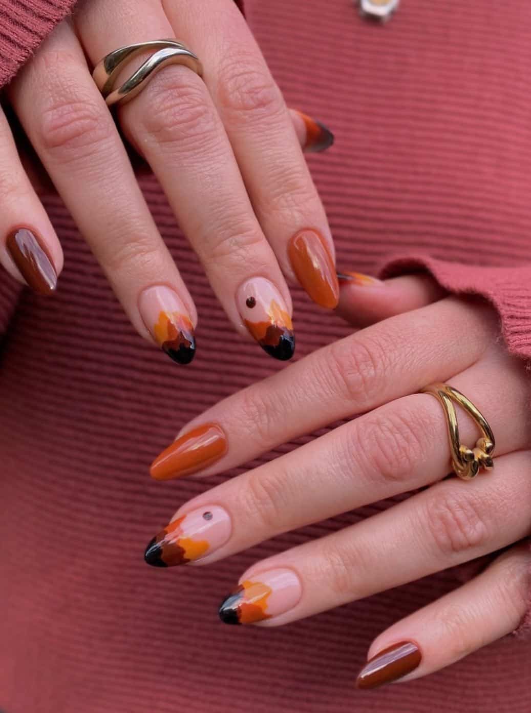 a hand with medium length almond nails painted in solid-colored brown and burnt orange with accent nails featuring mountain inspired nail art