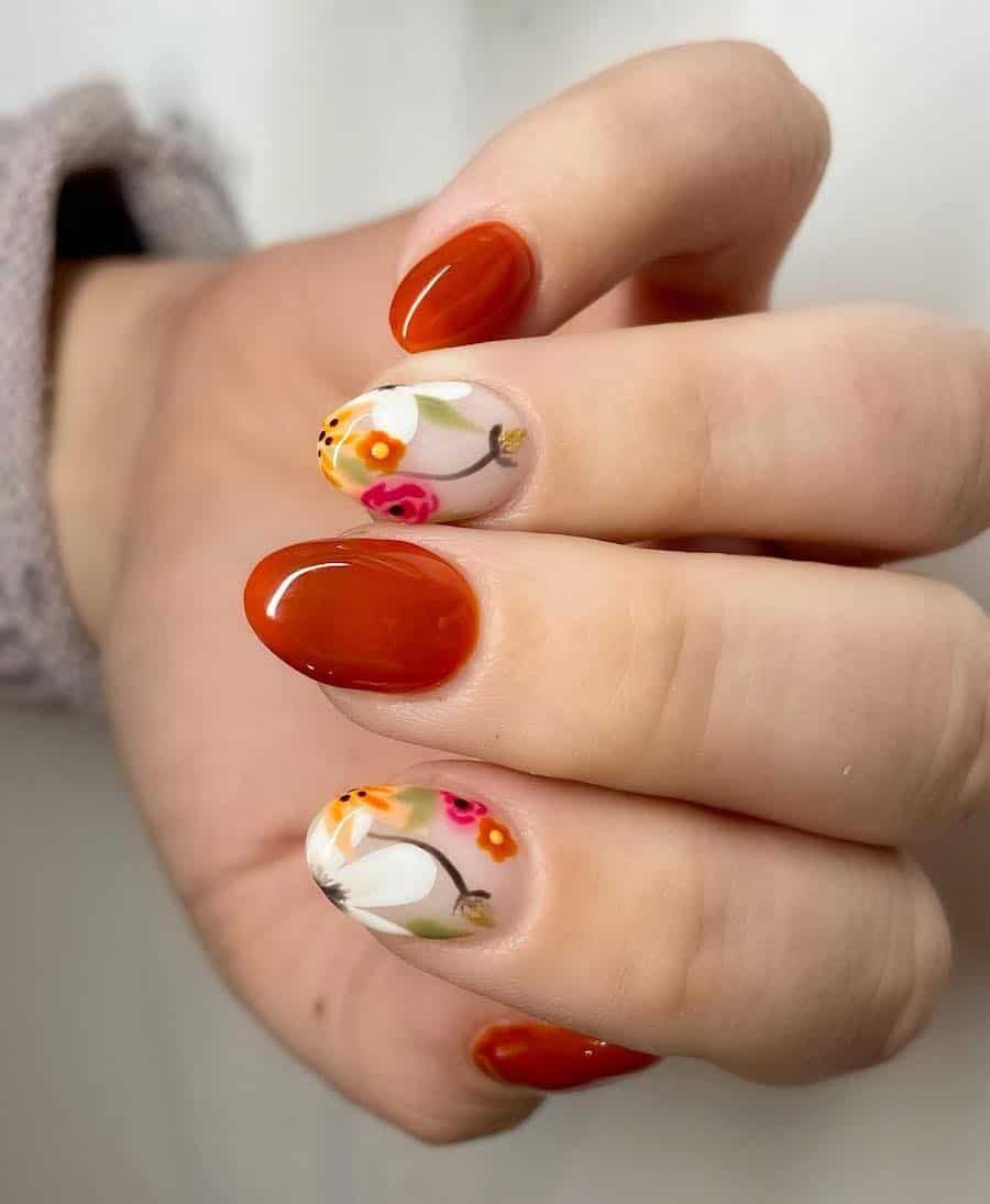 a hand with short round nails painted solid-colored burnt orange and nude glossy accent nails with colorful floral nail art