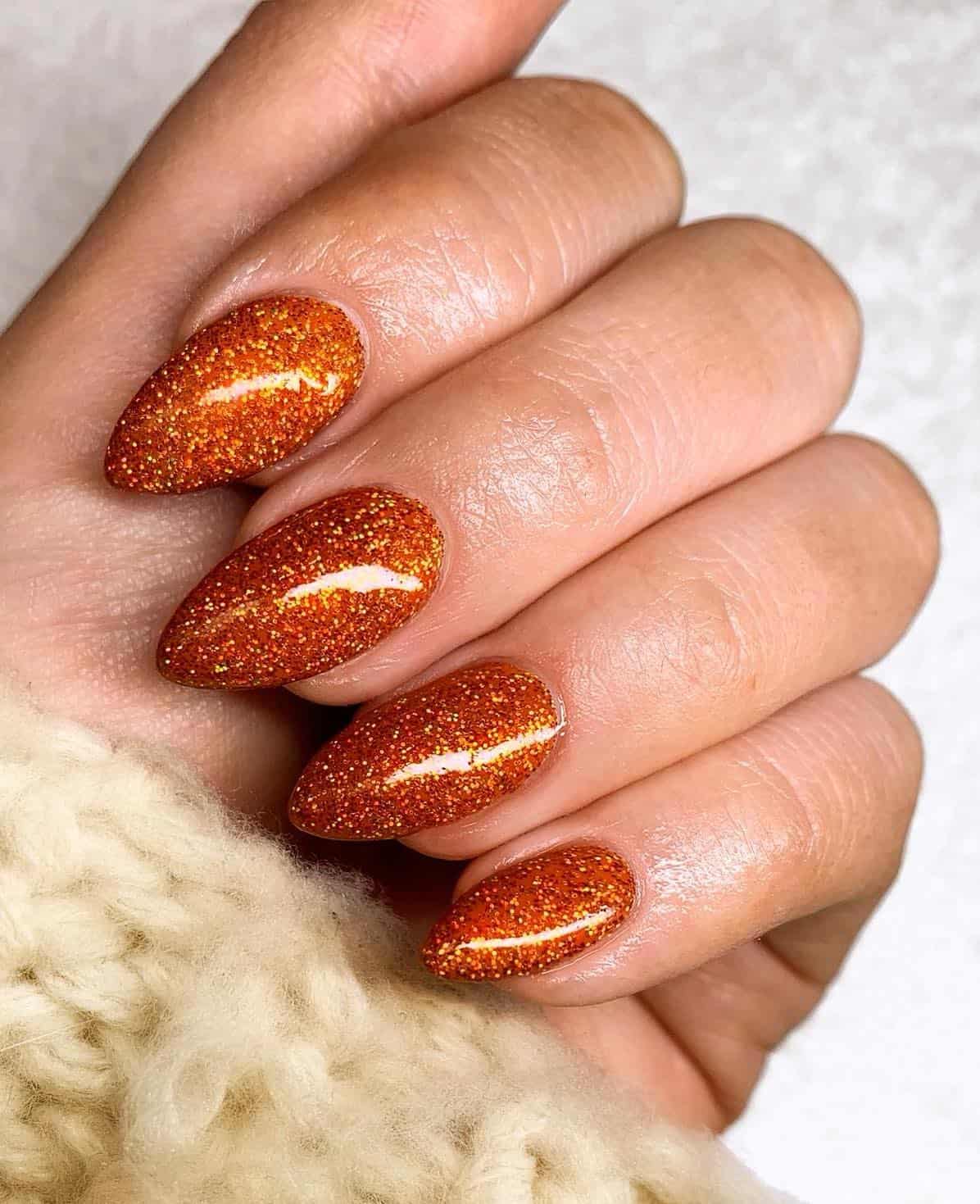 a hand with medium length glittery burnt orange polish