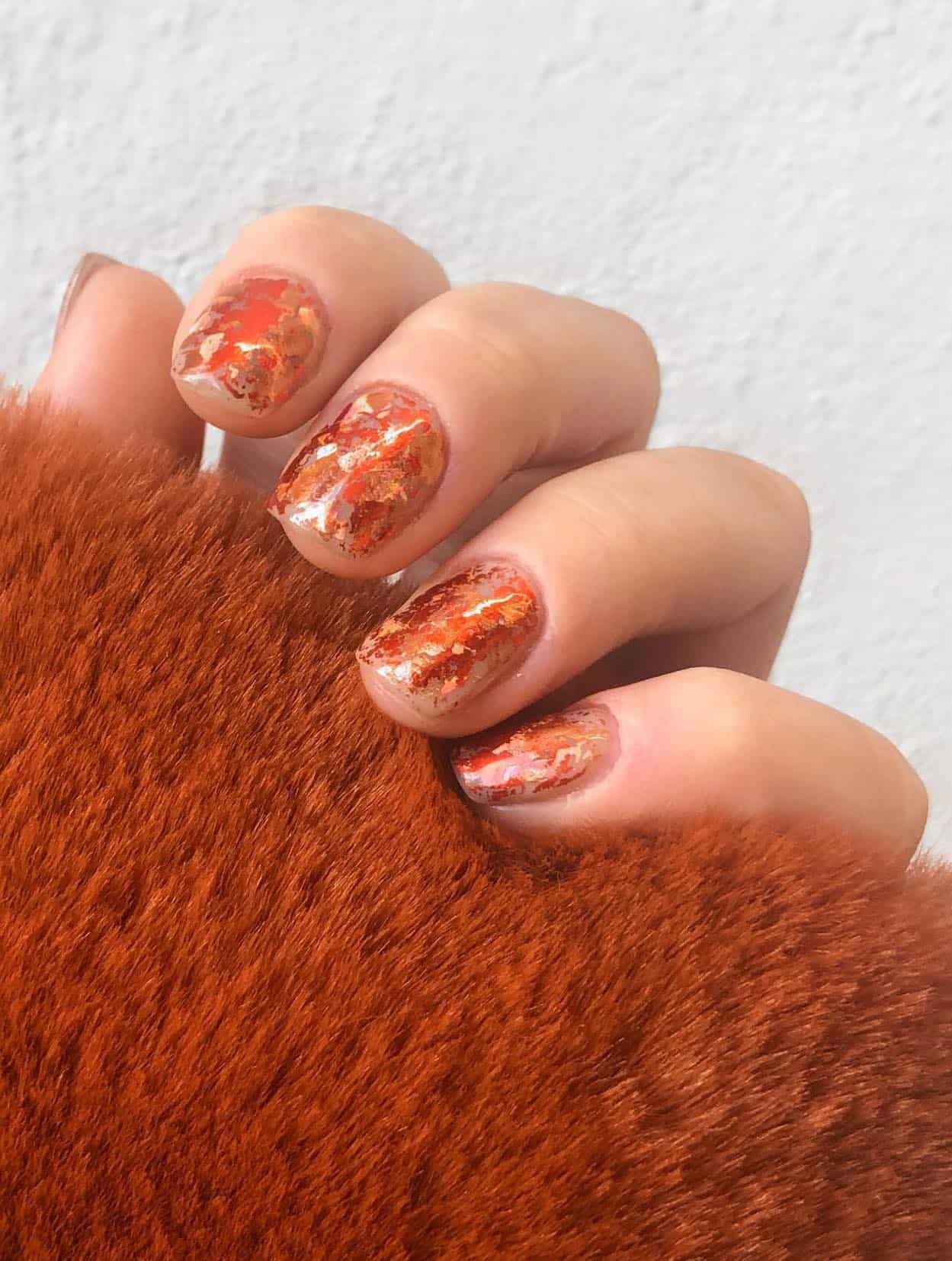 a hand with short square nude nails with burnt orange metallic flakes