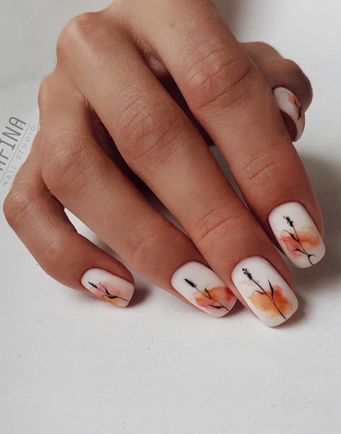 a hand with short white nails featuring an abstract burnt orange splotch and black floral art