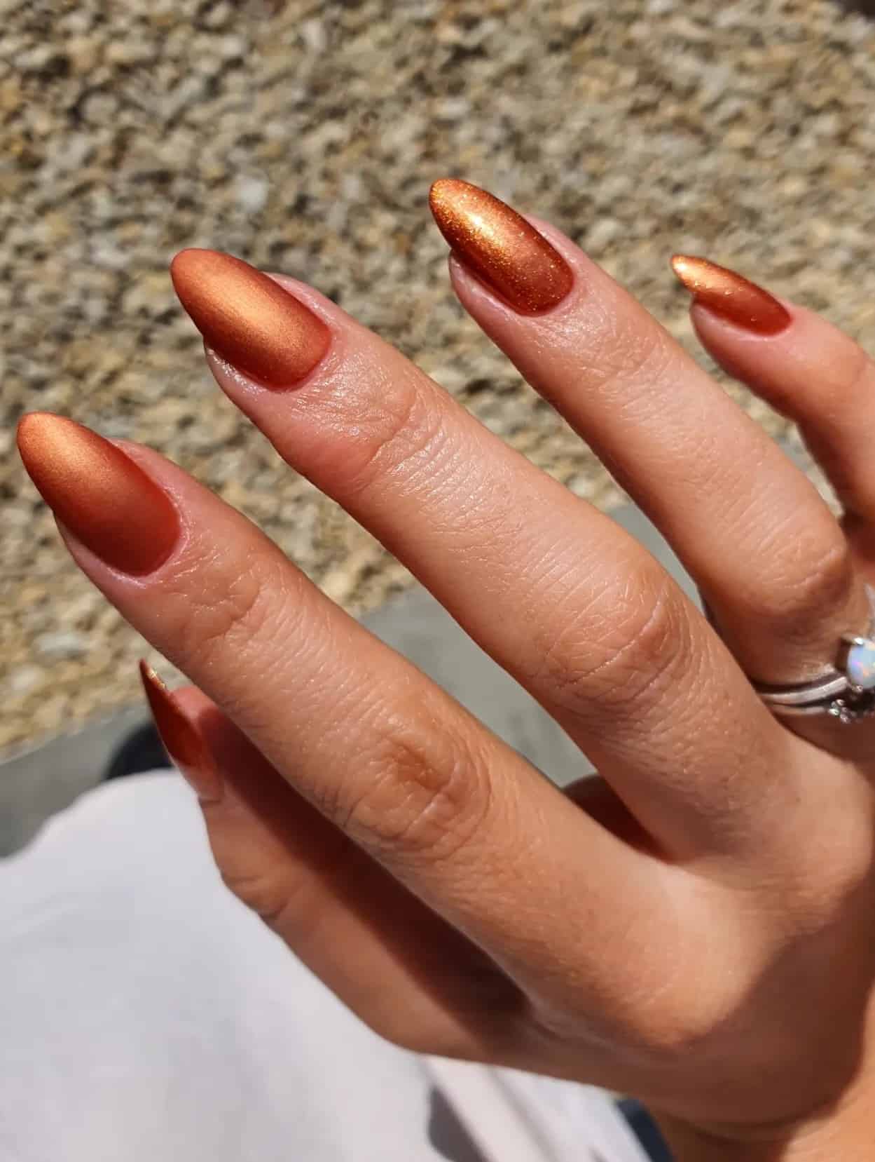 a hand with medium length nails painted burnt orange with a shimmering finish