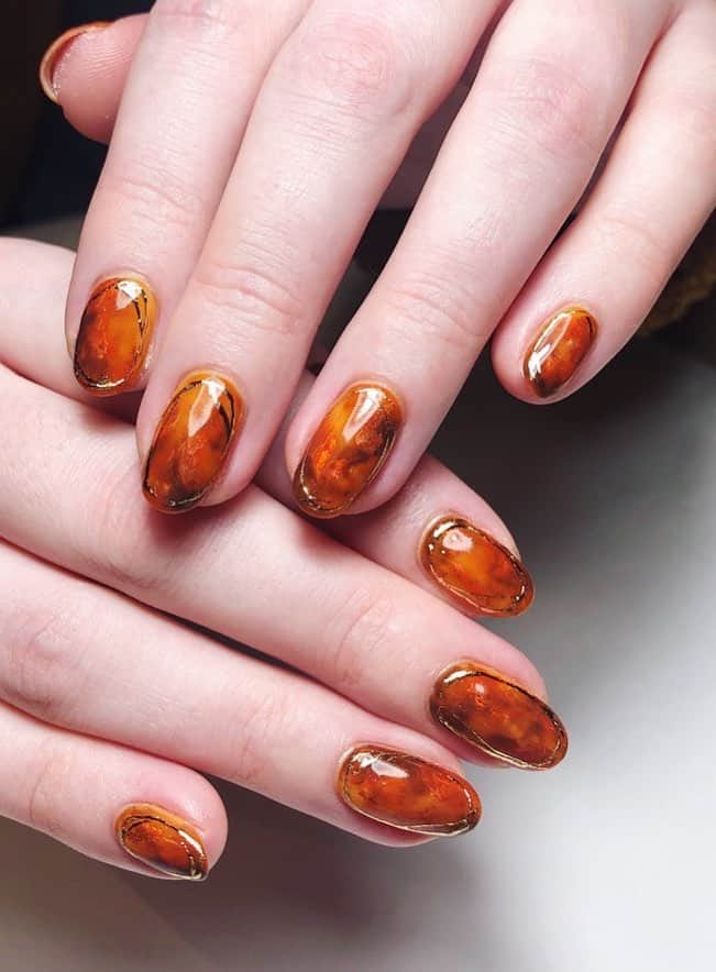 a hand with short round nails with a marbled burnt orange design and gold borders