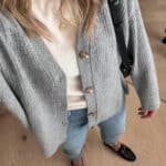 woman wearing a 2023 fall capsule wardrobe outfit with a grey knit cardigan over an ivory cashmere t-shirt with blue jeans and black loafers and a black crossbody bag