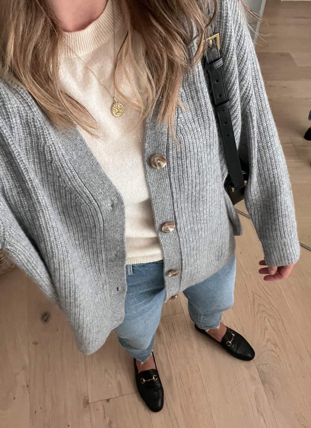 woman wearing a 2023 fall capsule wardrobe outfit with a grey knit cardigan over an ivory cashmere t-shirt with blue jeans and black loafers and a black crossbody bag