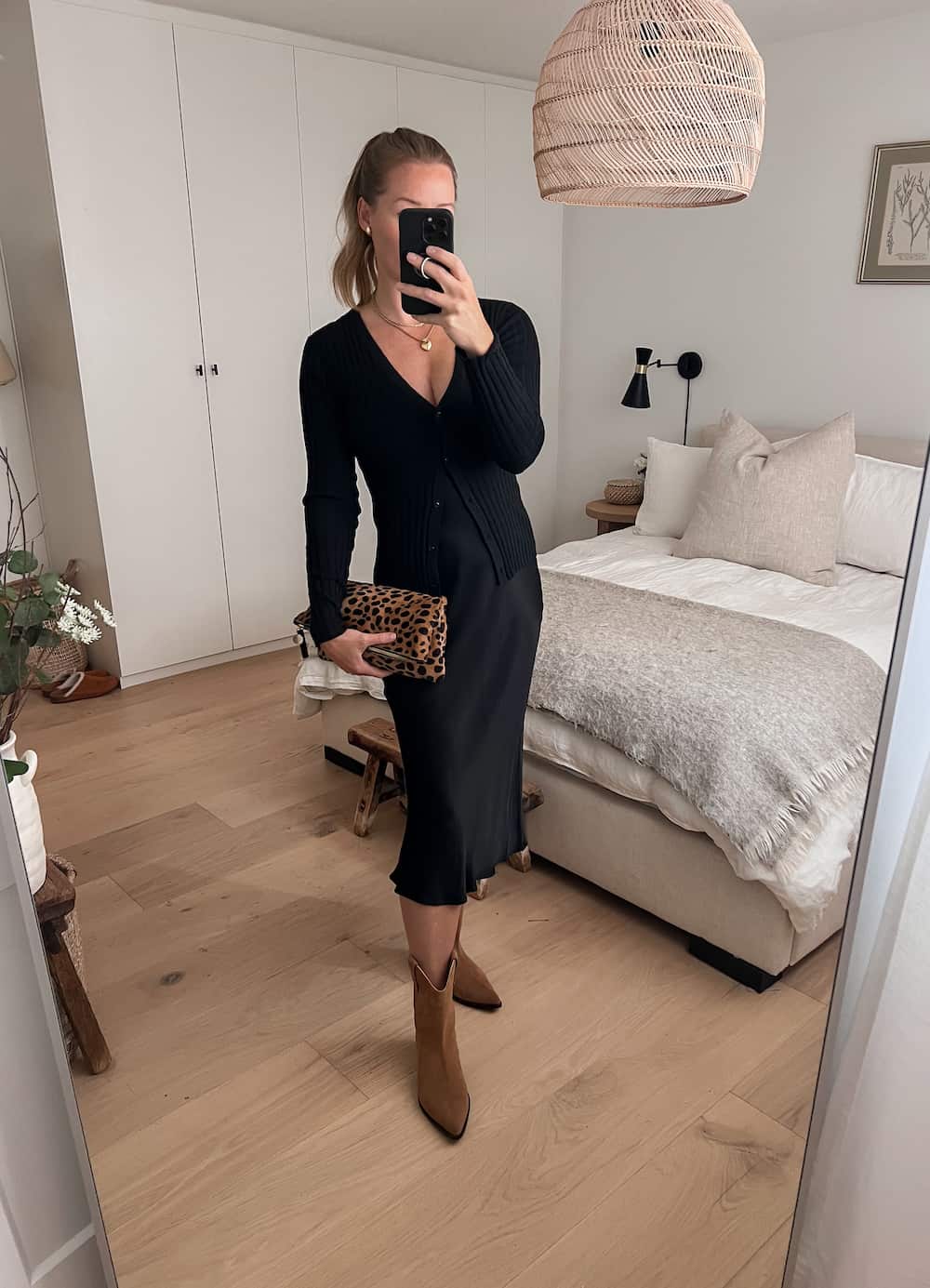 woman wearing a fall date night outfit with a black ribbed cardigan over a black slip dress and brown western style suede boots