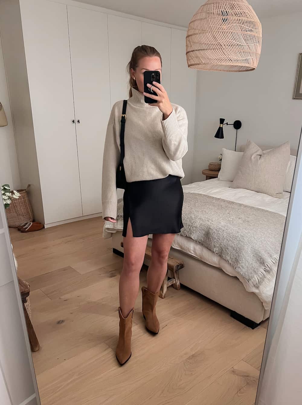 woman wearing a knit turtleneck sweater with a black slip mini skirt and brown suede western boots 