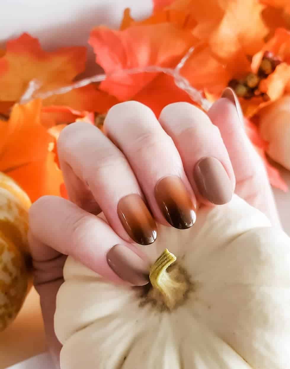 a hand with short glossy beige nails and two beige to brown ombre nails
