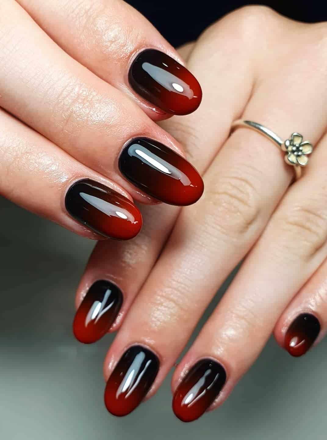 a hand with short round nails painted a glossy red and black ombre