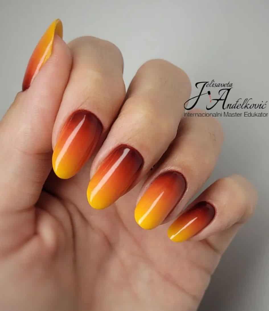 a hand with short round nails painted a yellow, orange, and red ombre