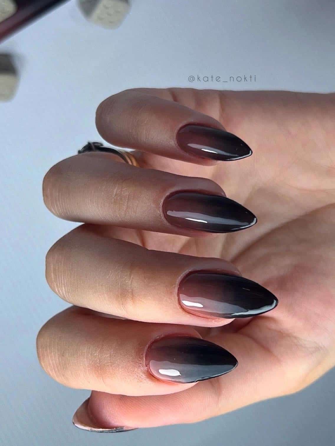 a hand with medium almond nails that have a brown and black ombre
