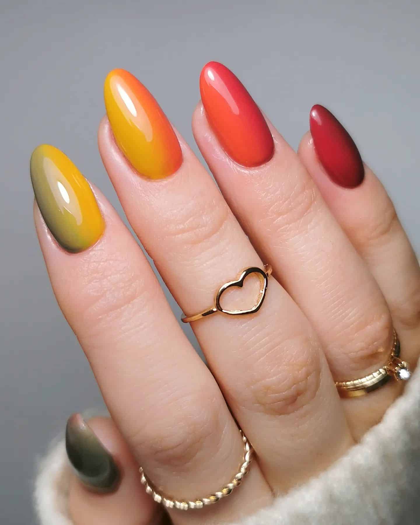 a hand with medium almond nails painted a horizontal ombre with dark green, yellow, orange, and red