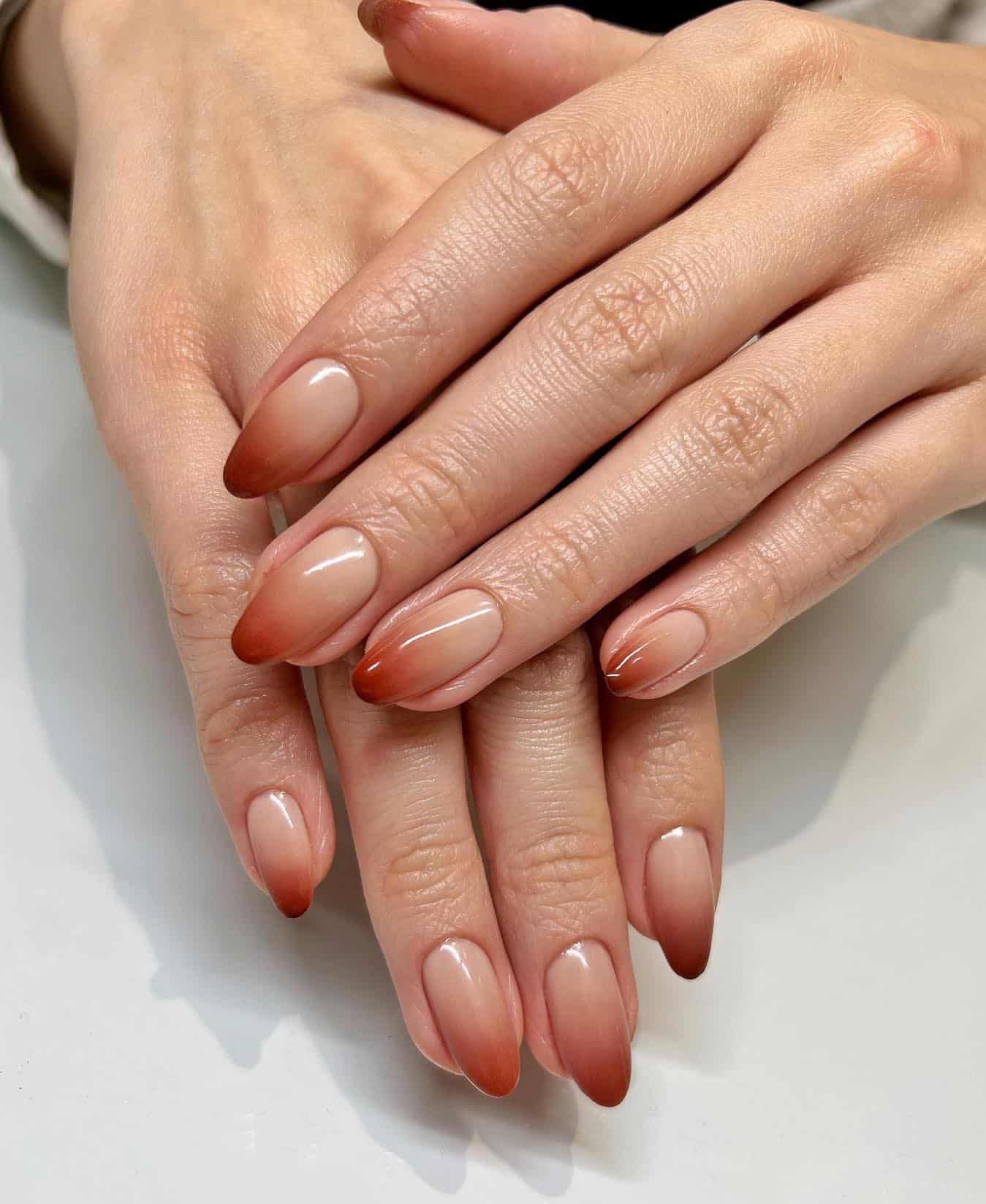a hand with short almond nails painted a nude to red ombre