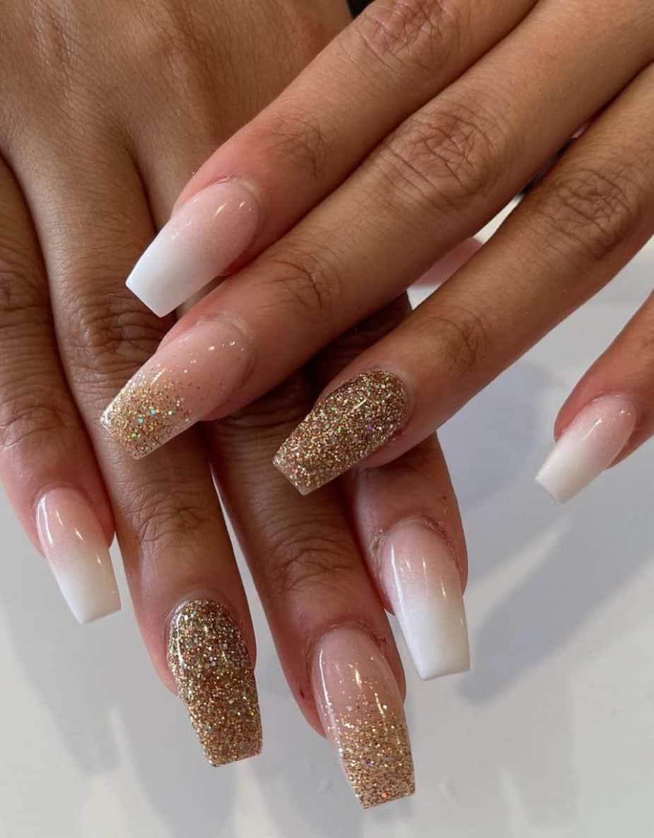a hand with medium coffin nails painted with nude and white ombre nails, gold glitter accent nails, and nude and gold ombre nails