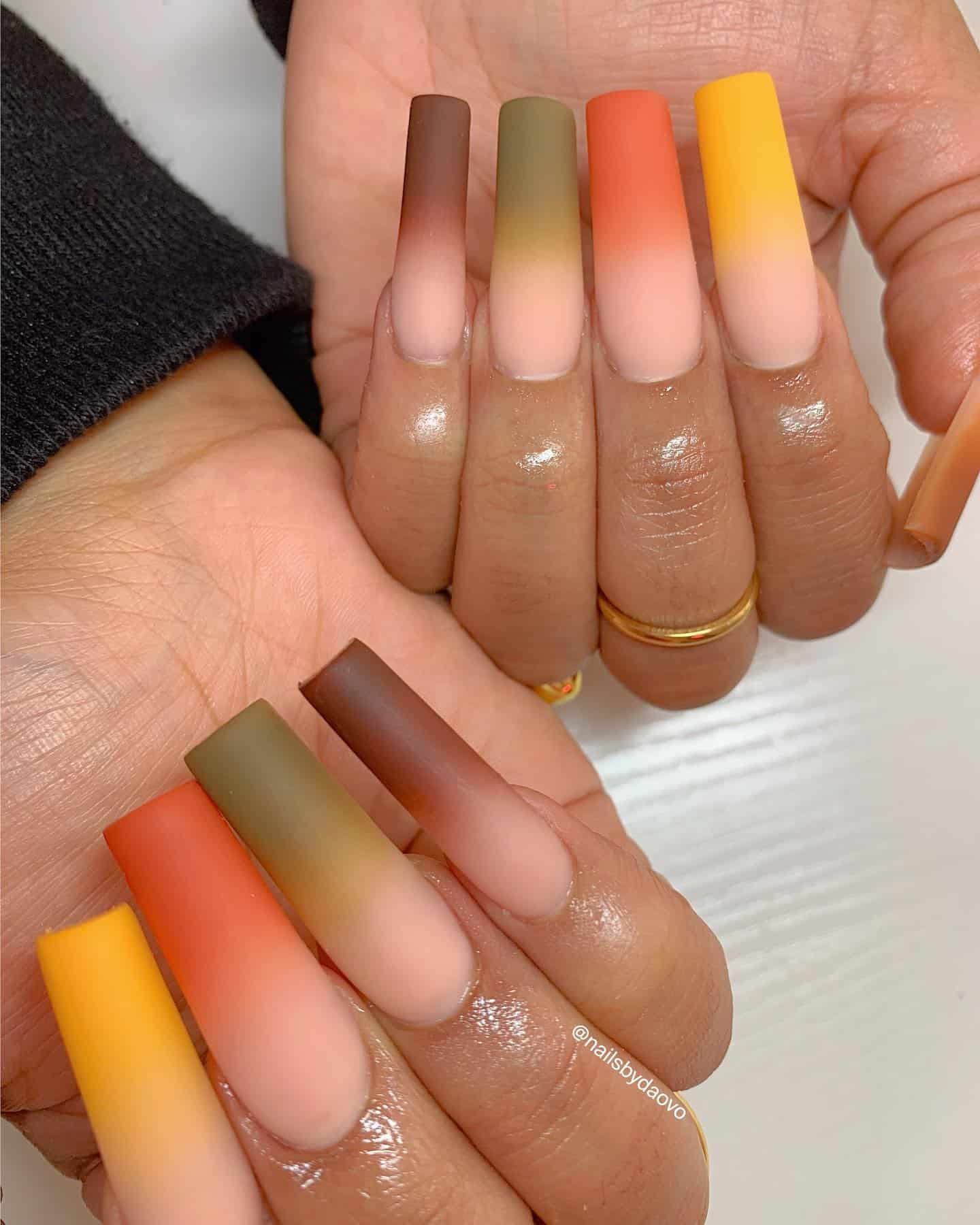 a hand with long square nails painted in matte ombre designs featuring brown, dark green, orange, and yellow