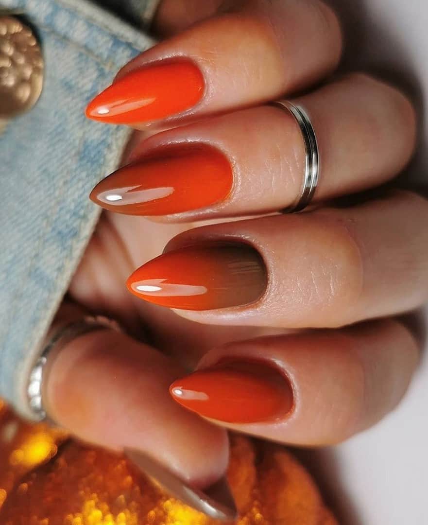 a hand with short stiletto nails painted an orange and burnt orange ombre