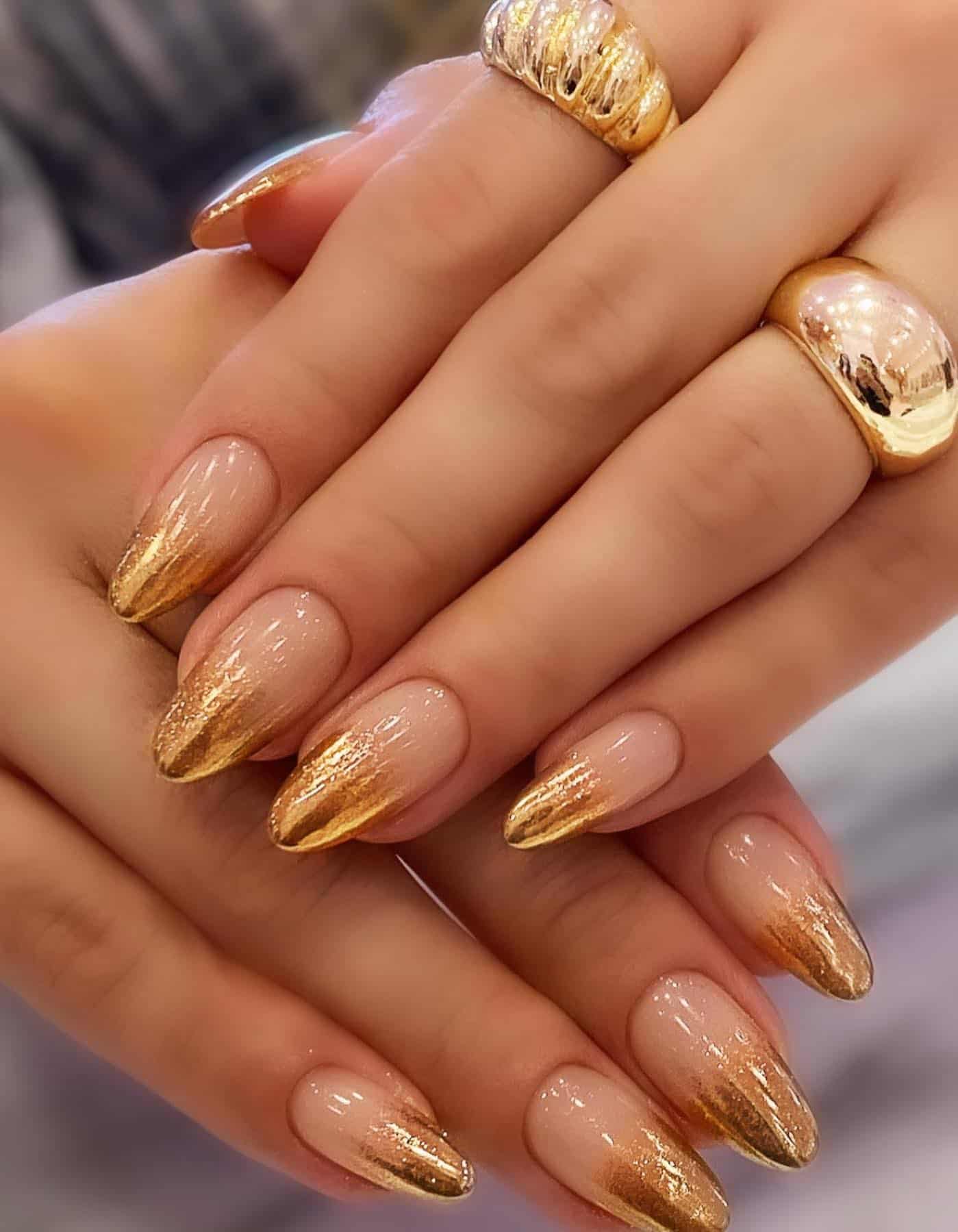 a hand with short almond nails painted a nude to gold ombre