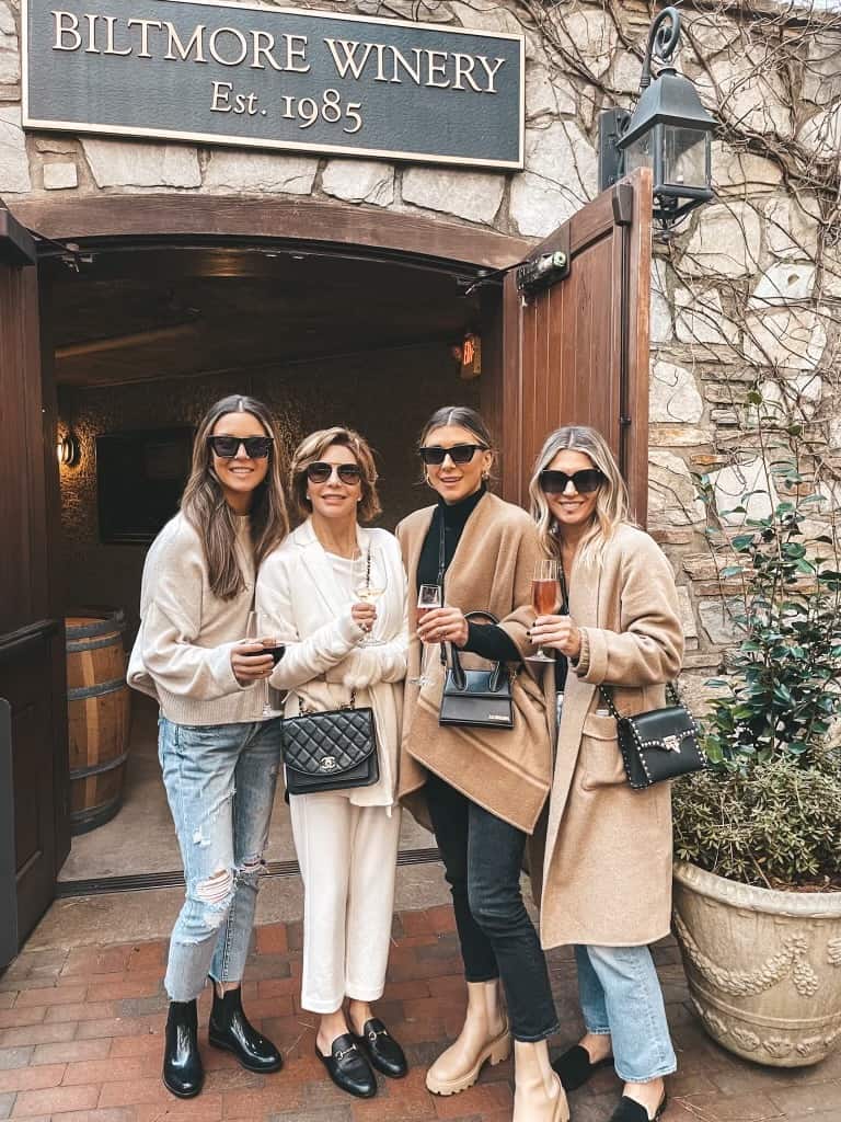a group of four women at a winery in the fall wearing jeans, boots, loafers, and long camel coats