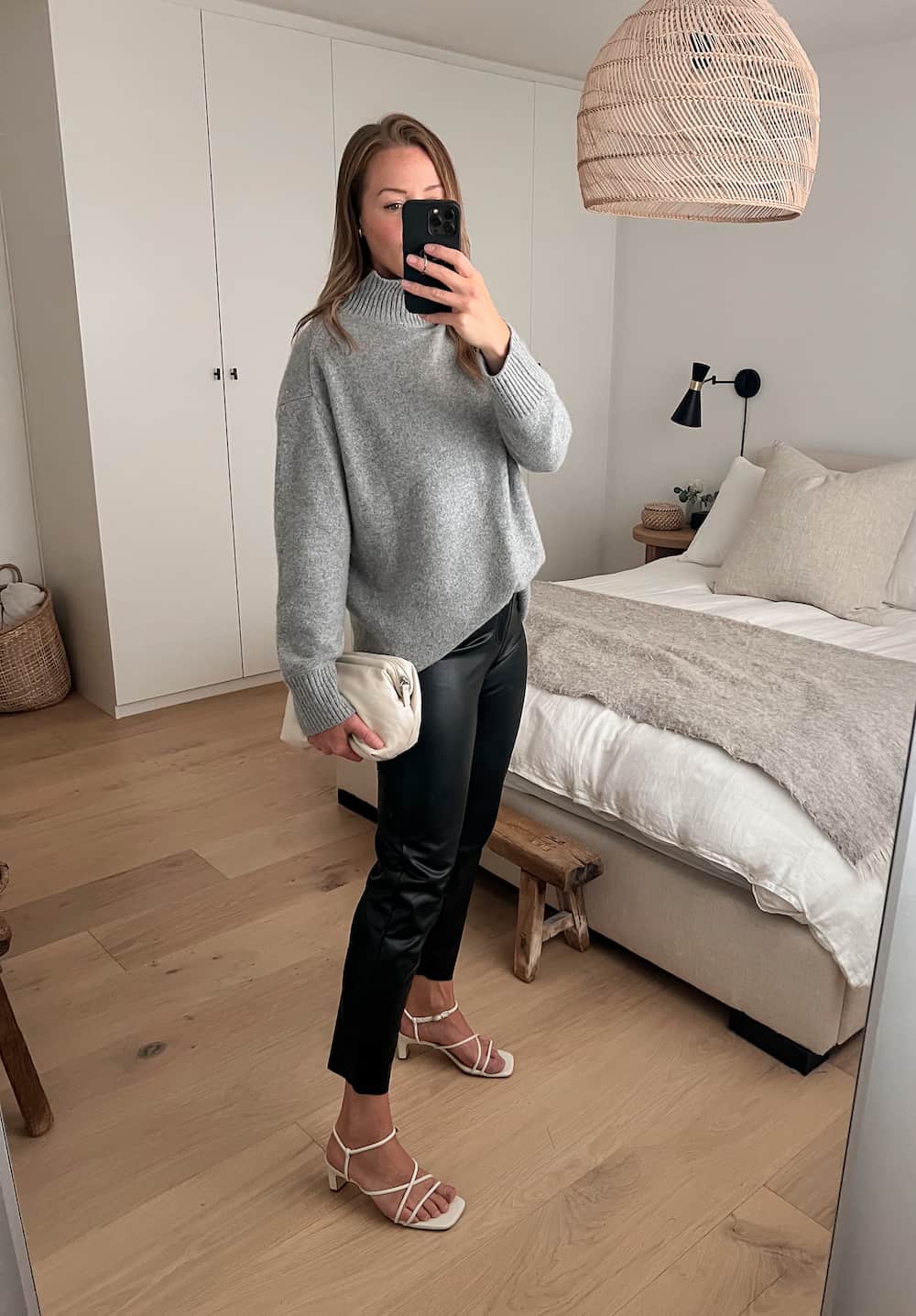 woman wearing an oversized grey turtleneck with black leather pants and while heeled sandals