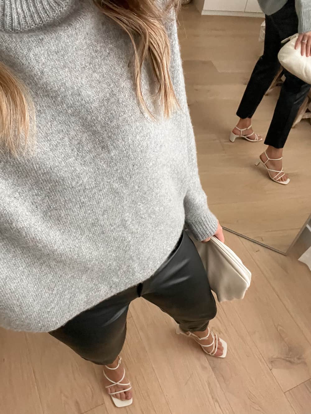 woman wearing a grey sweater with black leather pants and white heeled sandals