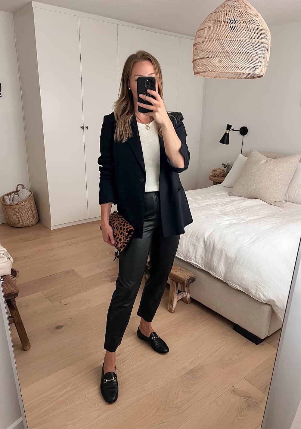 woman wearing a black blazer over an ivory knit top with black leather pants and Gucci loafers