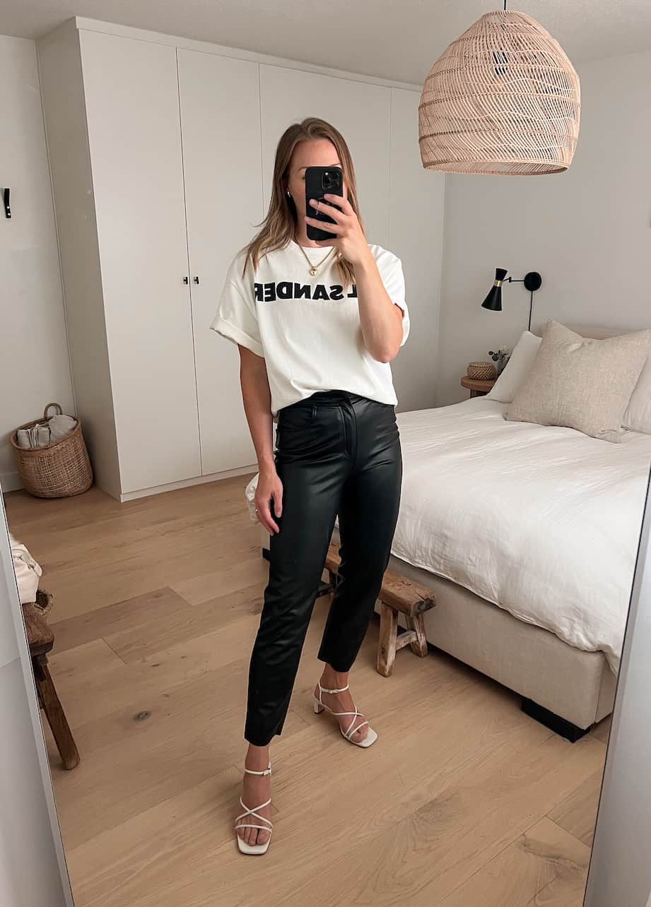 woman wearing an oversized white Jil Sander t-shirt with leather pants and white heeled sandals