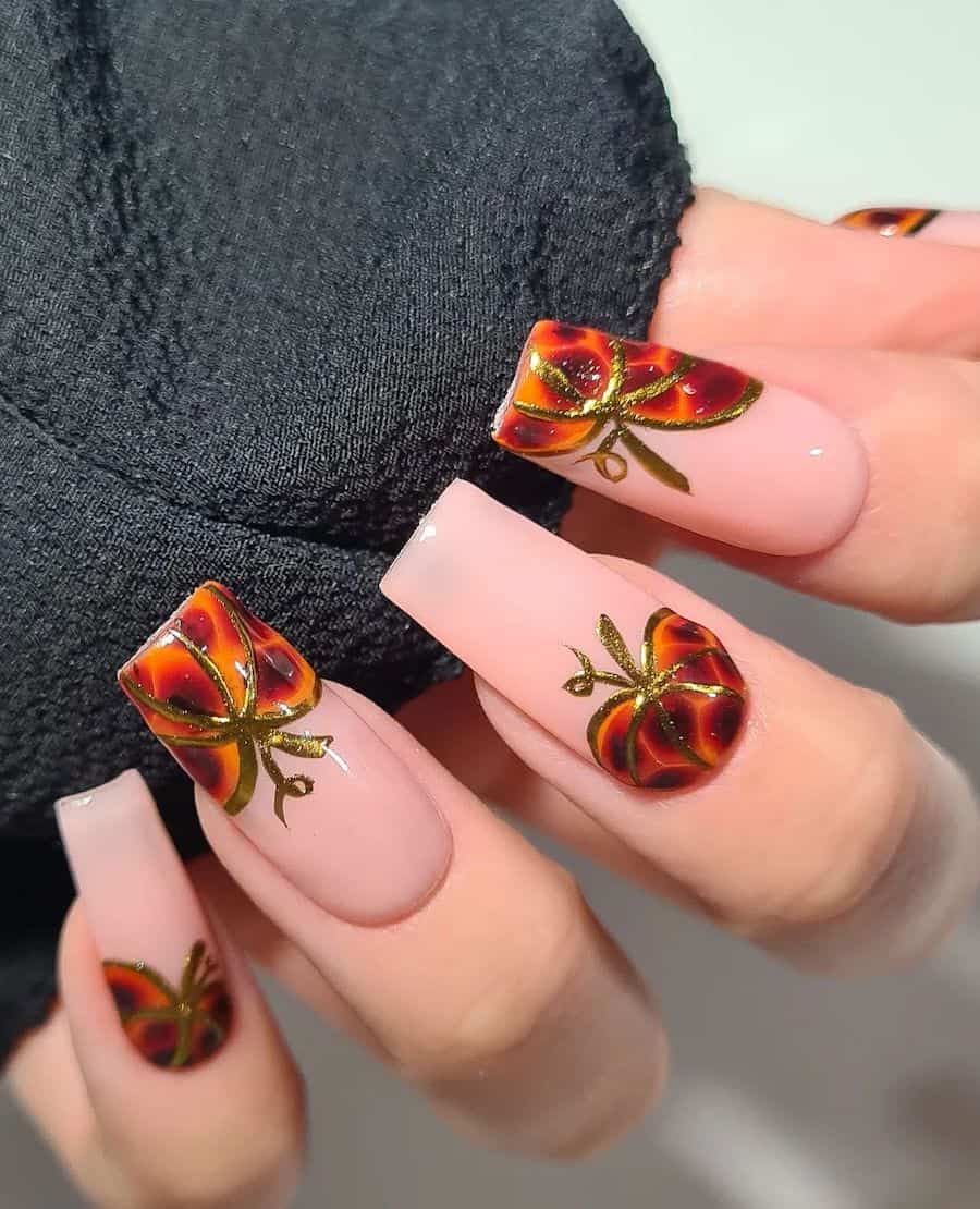 a hand with long square nails painted a glossy pastel pink with orange and brown pumpkins and gold stems