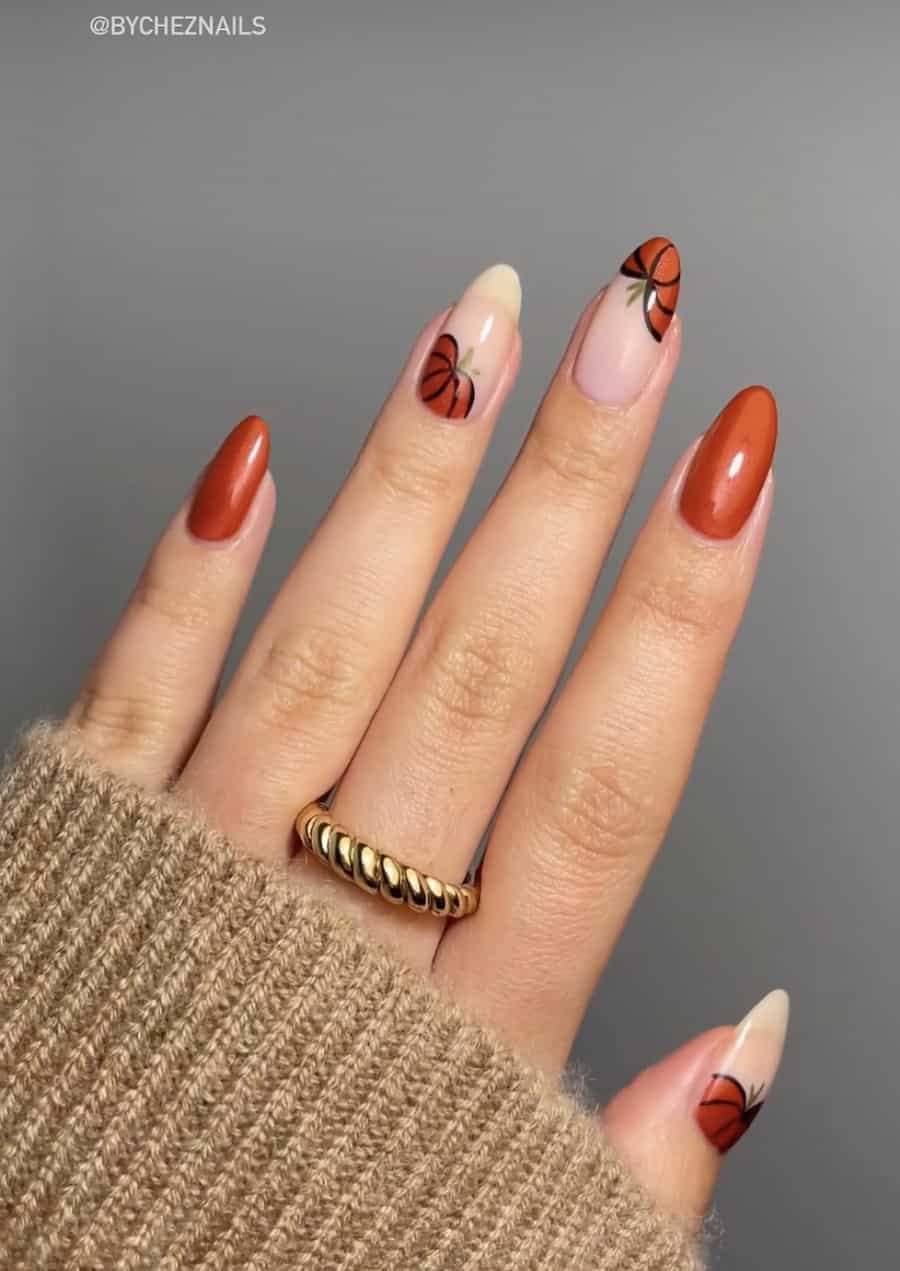 a hand with short almond nails painted a shimmering burnt orange with pumpkin art accent nails