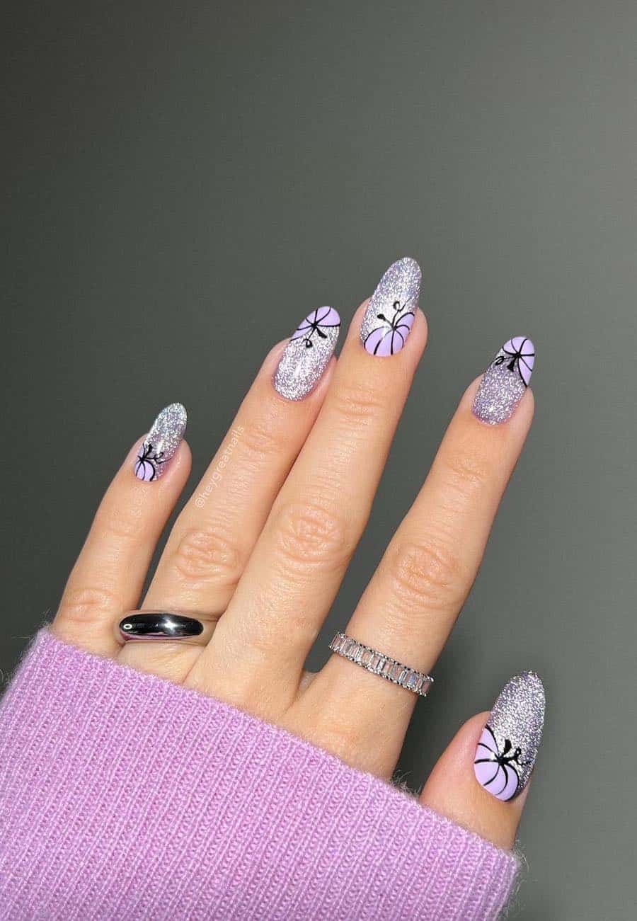 a hand with medium almond nails painted a silver slitter polish with purple pumpkin accent art