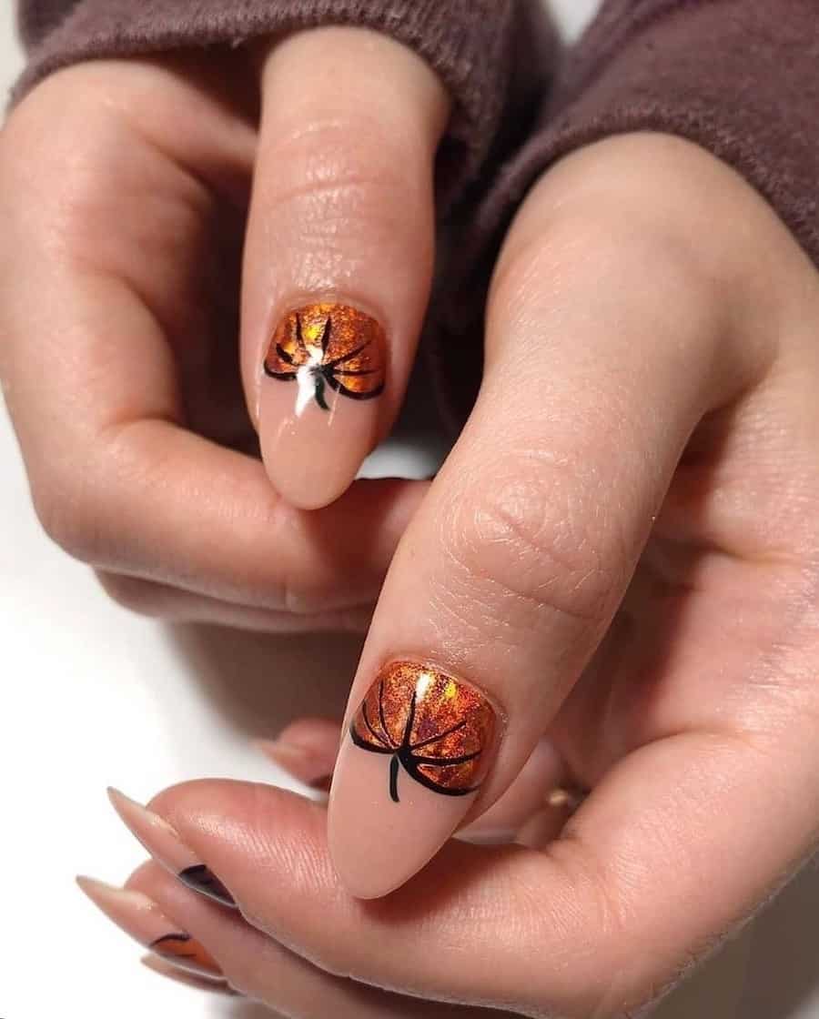 a hand with glossy nude almond nails with shimmering orange pumpkins painted at the base