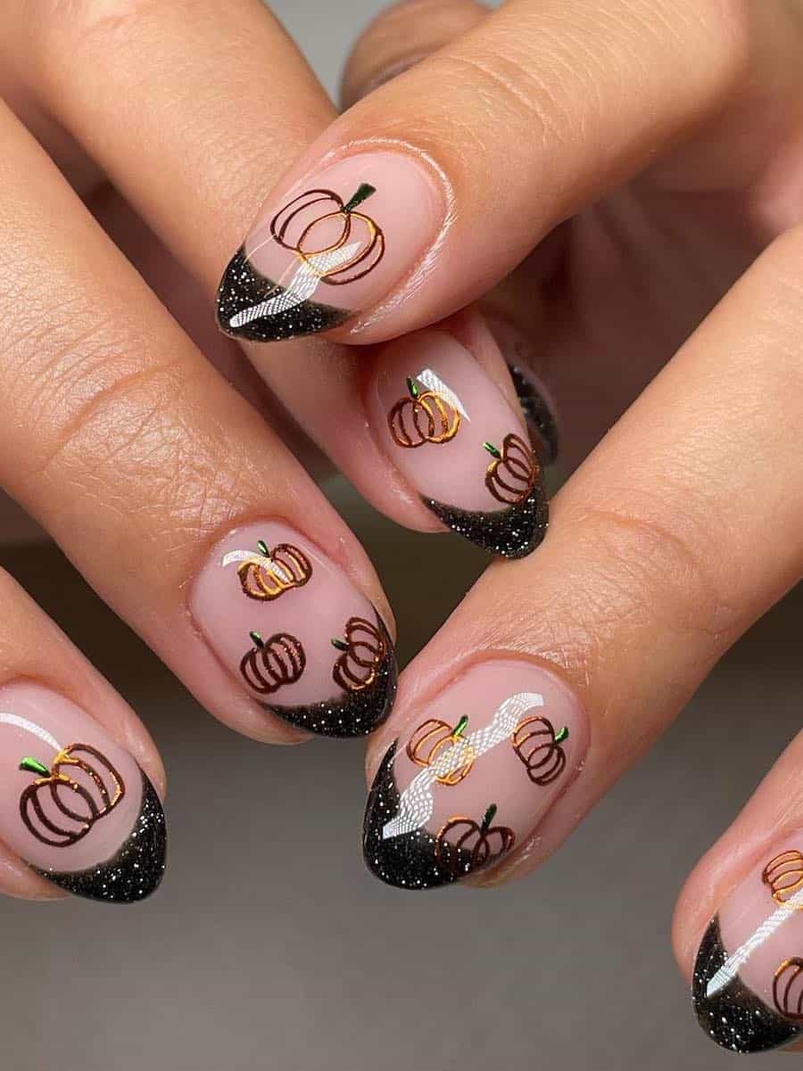 a hand with short round nails painted with sparkly black French tips and gold pumpkins