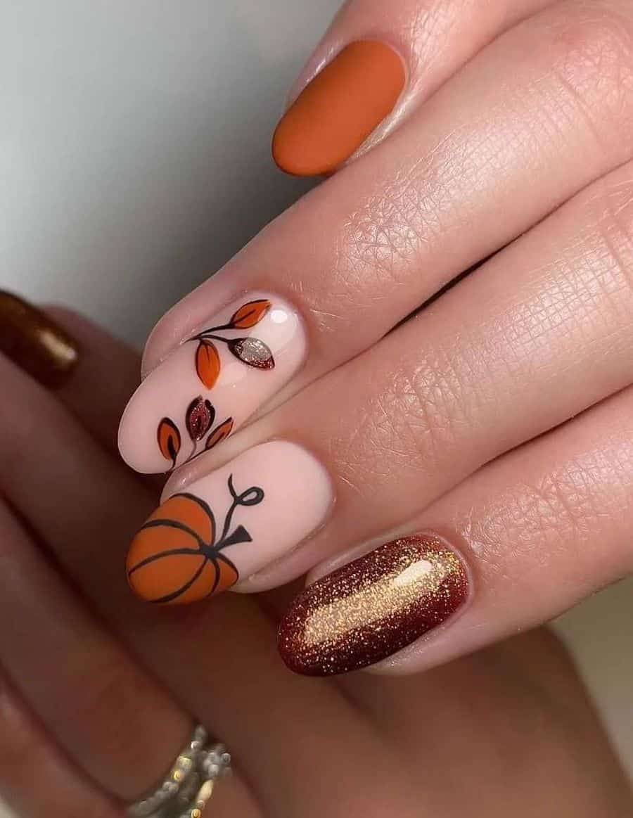 a hand with medium round nails painted a glossy nude with pumpkin and fall leaf nail art and accent nails with matte dark orange and copper-colored glitter polish